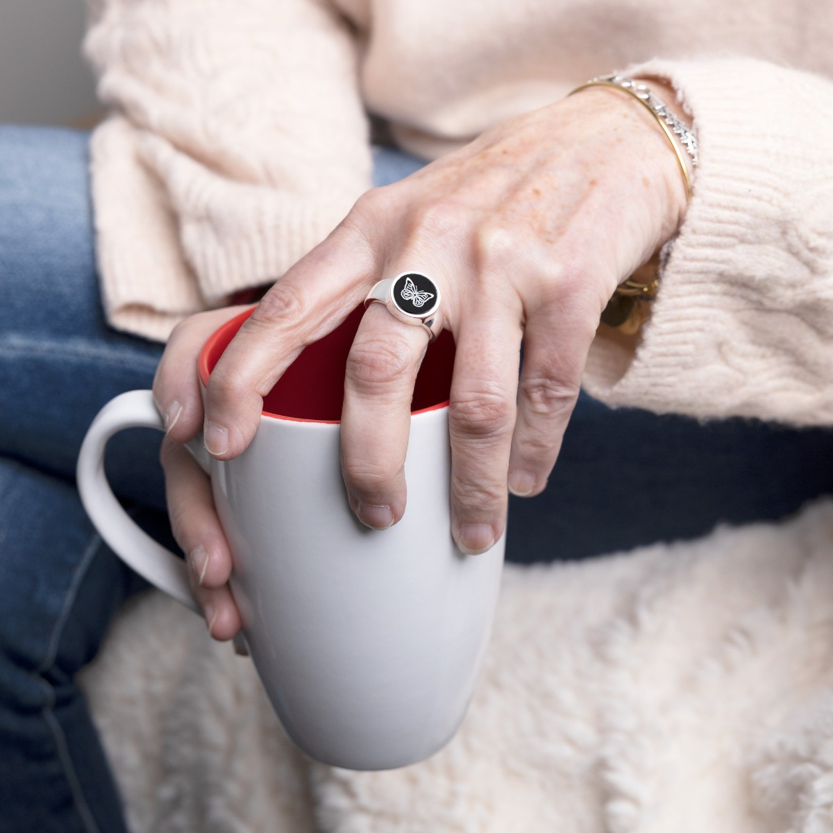 Woman holding cup of coffee with cremation ring on.