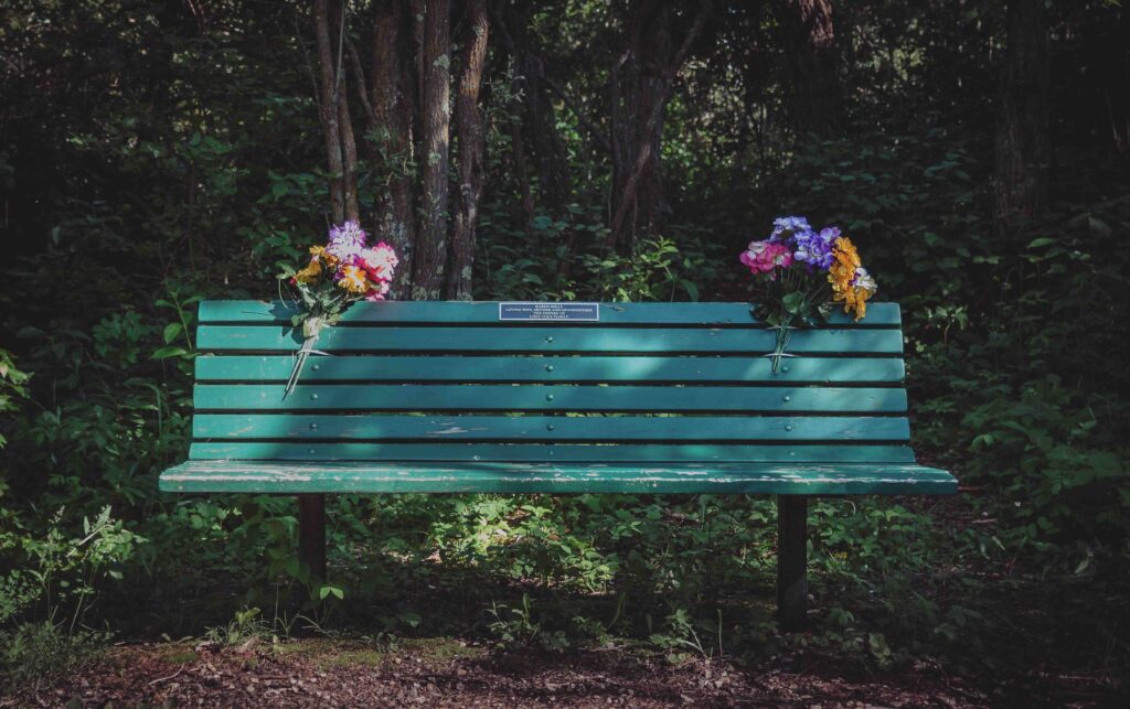 Teal memorial bench with flowers.